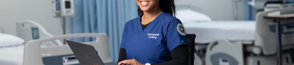 Nursing student sitting in a chair holding their laptop and smiling