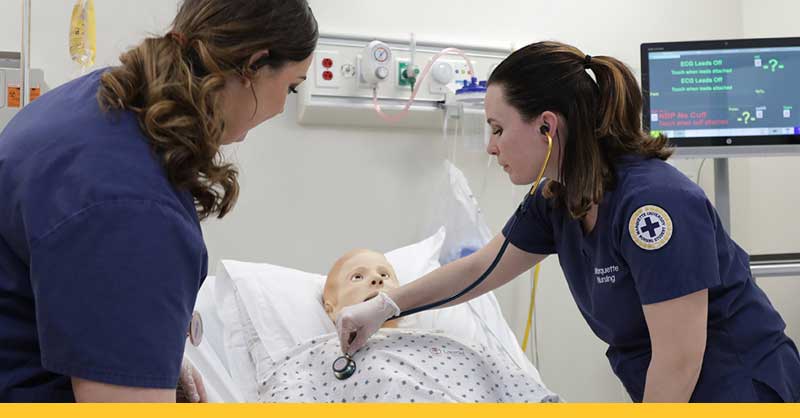 two nursing students working with a sim manikin